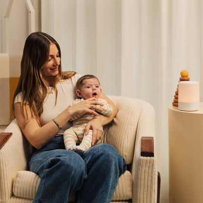 #alt_Mum smiling and sitting down while holding baby and baby looking at nanit sound + light 
